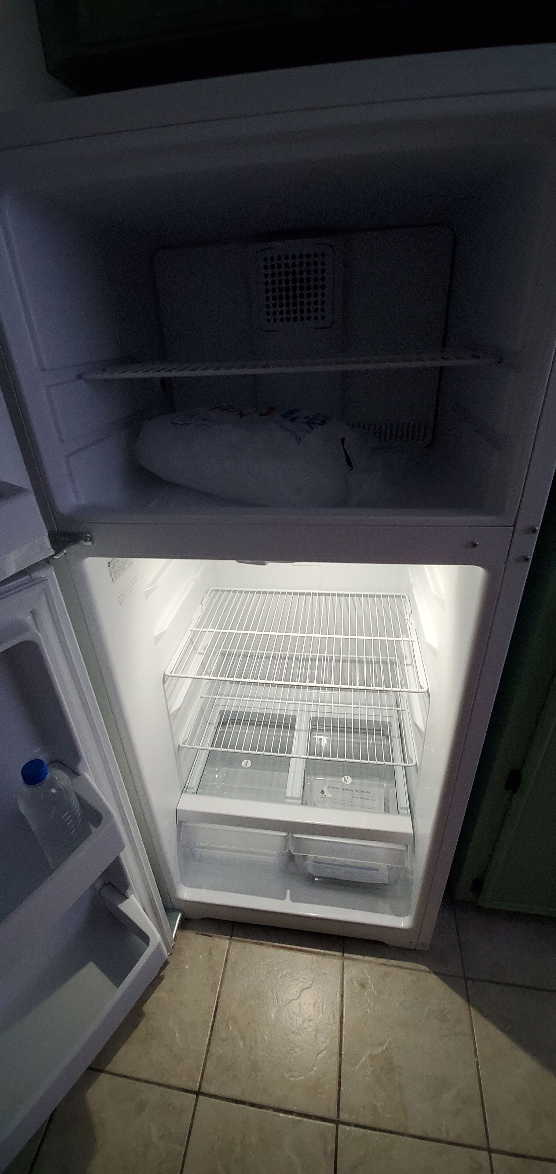 An open refrigerator with a water dispenser, a freezer compartment, and a shelf.