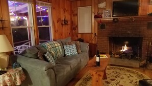 Un salon chaleureux avec un canapé gris, une table basse en bois, une cheminée et un téléviseur fixé au-dessus.