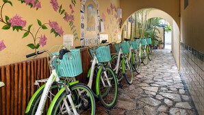 A row of bicycles parked against a wall with floral murals, a stone-tiled floor, and an arched corridor.