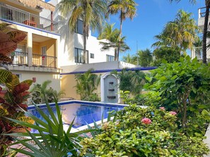 A hotel with a pool surrounded by tropical plants and palm trees.
