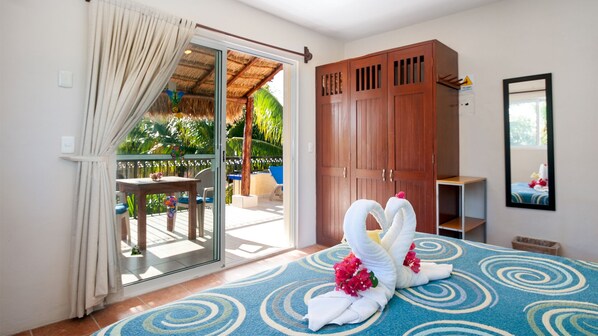 A hotel room with a sliding glass door leading to a balcony with a pool, a wooden wardrobe, and a bed with decorative swans and flowers.