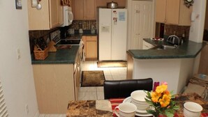 Une cuisine compacte avec des meubles en bois, un réfrigérateur blanc et un coin repas avec une table dressée pour deux personnes.