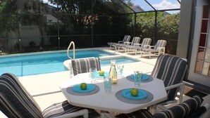 Un espace piscine extérieur avec une table pour deux, entouré de chaises longues à rayures.