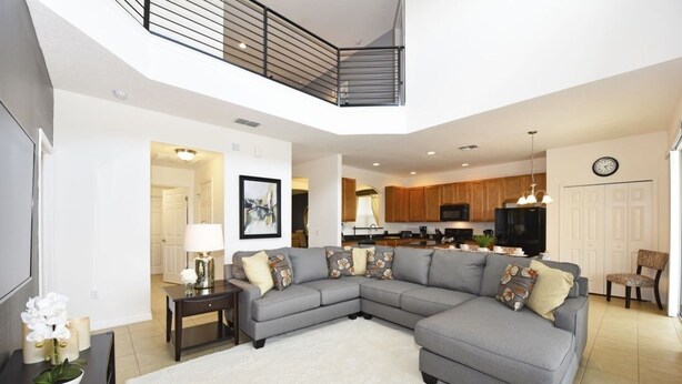 A modern living room with a grey sectional sofa, a white rug, and a kitchen in the background. - Providence At Crofton Springs 6 Bedroom Home by RedAwning (Davenport)