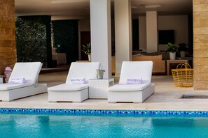 A poolside area with three white lounge chairs, each with a towel and a pillow labeled "Beachrock."