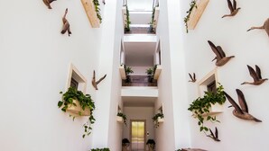 En smal, flera våningar hög korridor med vita väggar, träskåp och krukväxter.