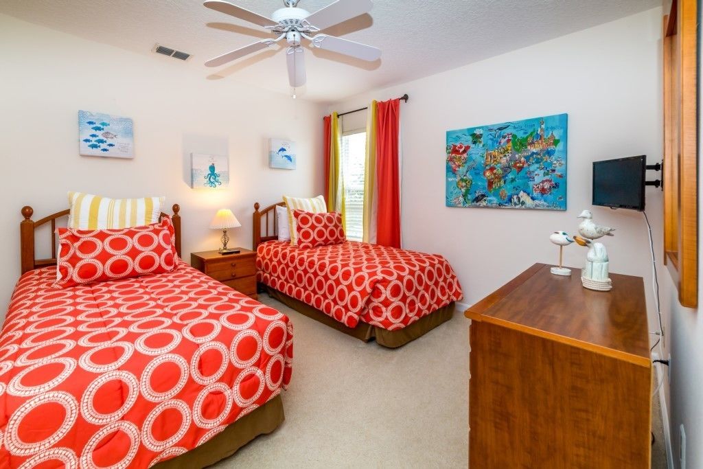 A bedroom with two beds, a ceiling fan, a nightstand with a lamp, a dresser, and a wall map.