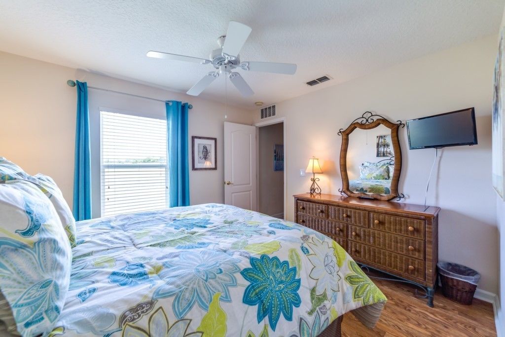 A bedroom with a bed, a dresser, a ceiling fan, a television, and a window with curtains.