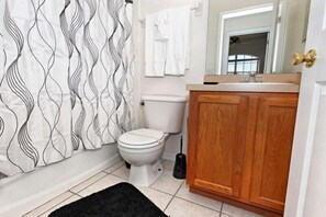 Un baño con inodoro, un mueble de madera, un tapete negro y una cortina de ducha con un diseño ondulado.