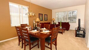 A dining area with a wooden table set for four, flanked by chairs. A sofa and a red armchair are positioned in the background. - 684od 5 Bedroom Home by RedAwning (Davenport)