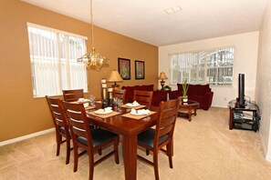 A dining area with a wooden table set for four, a sofa, and a TV stand with a fireplace.