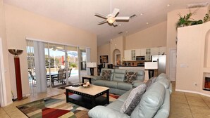A spacious living room with a light blue sofa, a coffee table, and a colorful rug. There is a ceiling fan, a dining area with chairs, and a kitchen in the background. - 351bs 5 Bedroom Villa by RedAwning (Davenport)