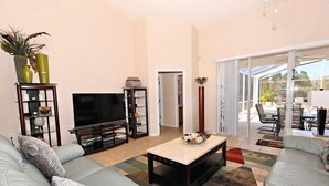 A living room with a sofa, TV, coffee table, and a view of the outdoor patio area. - 351bs 5 Bedroom Villa by RedAwning (Davenport)
