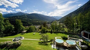 A mountainous landscape with a pool area featuring hot tubs and a view of a valley with houses.