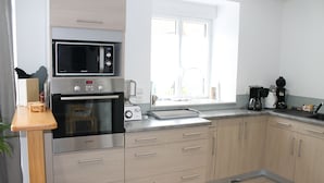 Une cuisine moderne dotée d’appareils électroménagers en acier inoxydable, de meubles en bois et d’une fenêtre laissant entrer la lumière naturelle.