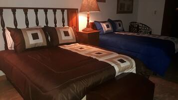 Un dormitorio con una cama grande, una cama más pequeña, una mesita de noche con una lámpara y un cabecero.