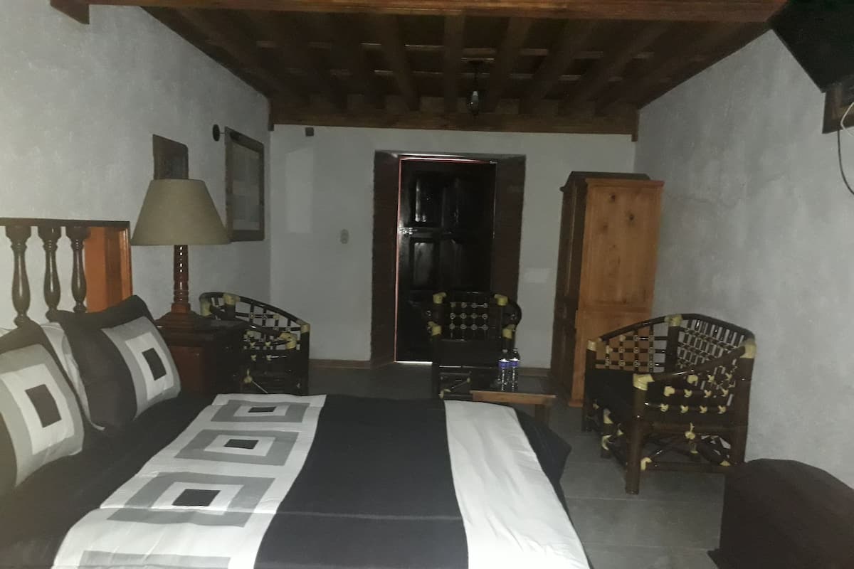 A bedroom with a bed, two chairs, a wooden cabinet, and a door leading to another room.