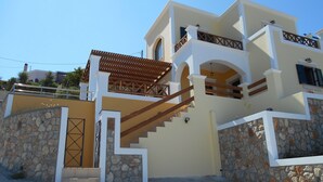 Uma casa moderna de dois andares com fachada de pedra, escadaria de madeira e varanda.