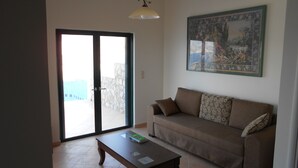 Uma sala de estar com sofá, mesa de centro, quadro na parede e porta de vidro deslizante para área externa.
