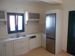Una cocina con armarios blancos, un refrigerador de acero inoxidable, un fregadero y una ventana con persianas.
