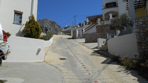 Uma rua estreita e pavimentada ladeada por edifícios brancos com detalhes em pedra, que se estende em direção a um cenário montanhoso.