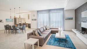 A modern living room with a sectional sofa, dining table, and chairs, a TV, and a large window with curtains.