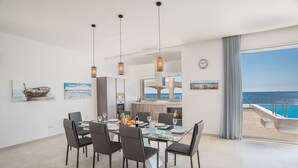 A modern dining area with a glass table, six chairs, and hanging pendant lights.