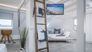 A modern loft bedroom with a loft bed, a TV mounted on the ceiling, a wooden ladder, and a potted plant. - Design - Studio in Gütersloh with balcony (Gütersloh)