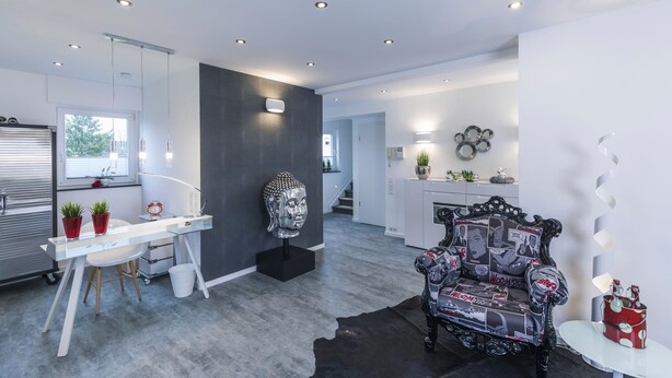 A modern living room with a white desk, a black chair with a patterned design, and a large Buddha head sculpture on a pedestal. - Design - Studio in Gütersloh with balcony (Gütersloh)