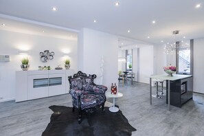 A modern kitchen with a central island, a dining area with a table and chairs, and a living space with a patterned armchair and a small side table.