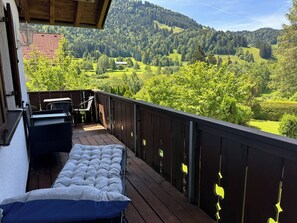 Un balcon aménagé avec un matelas, des chaises et une table, offrant une vue sur un paysage montagneux.