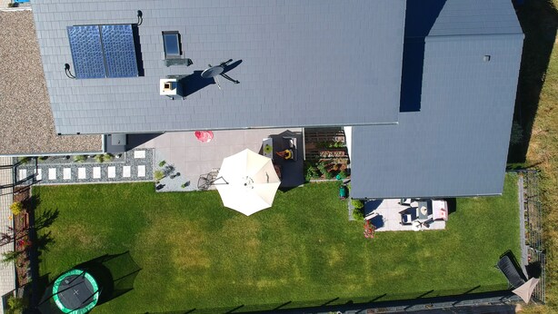 An aerial view of a house with a sloped roof, solar panels, a fenced yard, and a trampoline. - Modern apartment in a quiet location (Bischberg)