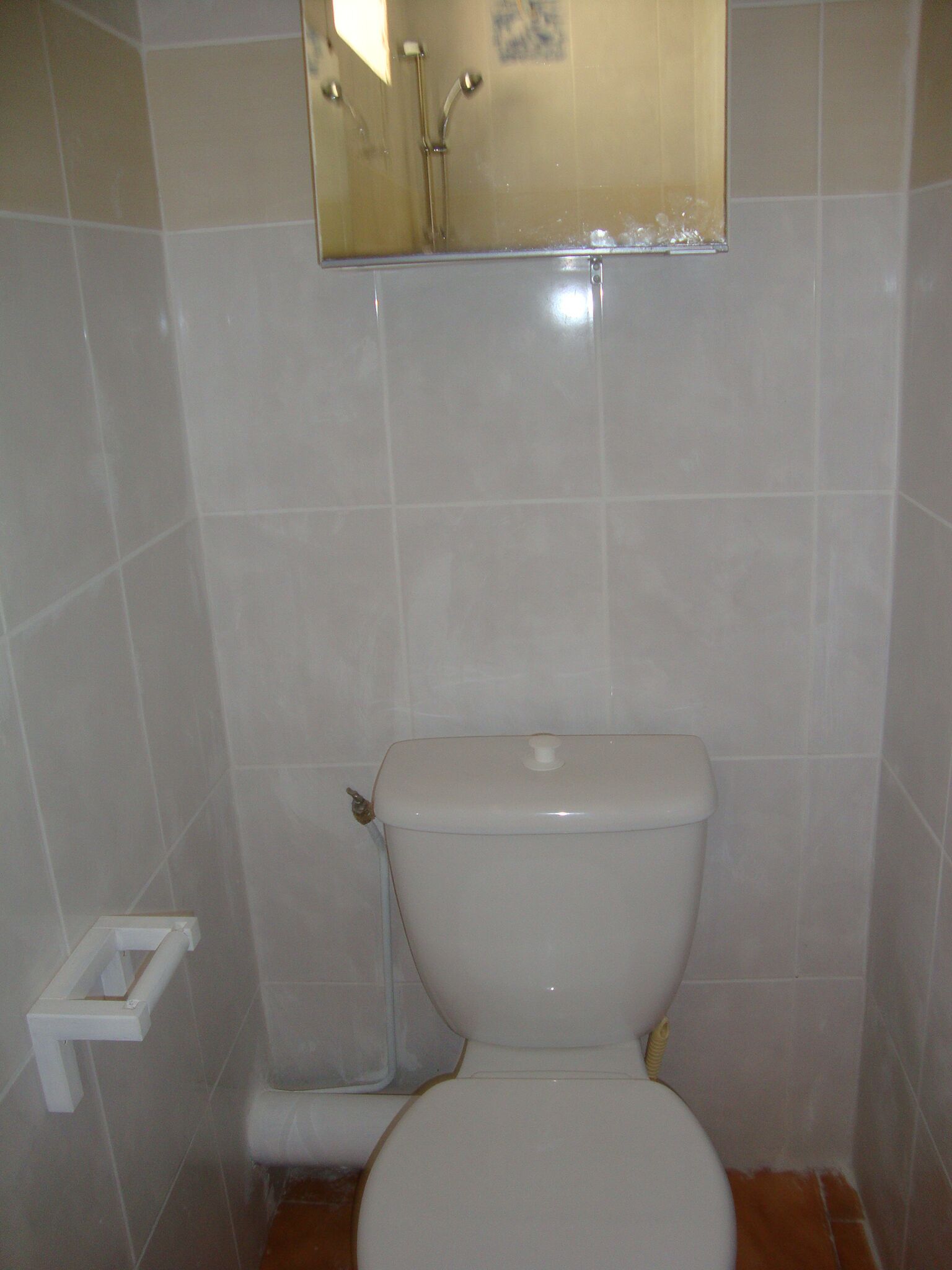 A bathroom with a toilet, a small mirror above it, and a toilet paper holder to the left.