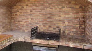 Una parrilla exterior de ladrillo con techo inclinado, rejilla metálica y superficie de cocción plana.