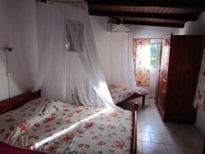 A bedroom with two beds, a wardrobe, and a window with floral curtains. - Welcome to Residence Madelia in Guadeloupe (Port-Louis)