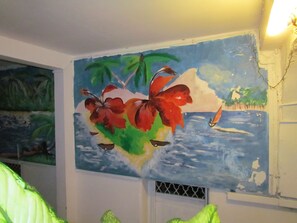 Features a vibrant mural with tropical elements, a window for natural light, and a simple layout.