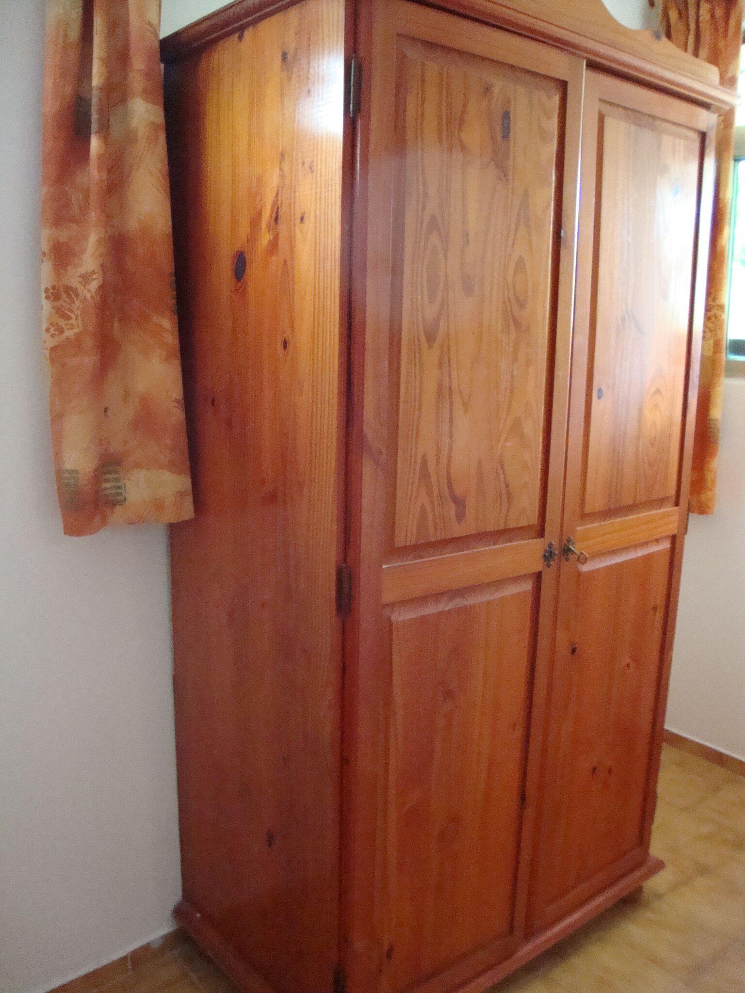 A wooden wardrobe with two doors and a handle, positioned against a wall with a window.