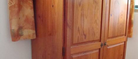 A wooden wardrobe with two doors and a handle, positioned against a wall with a window.