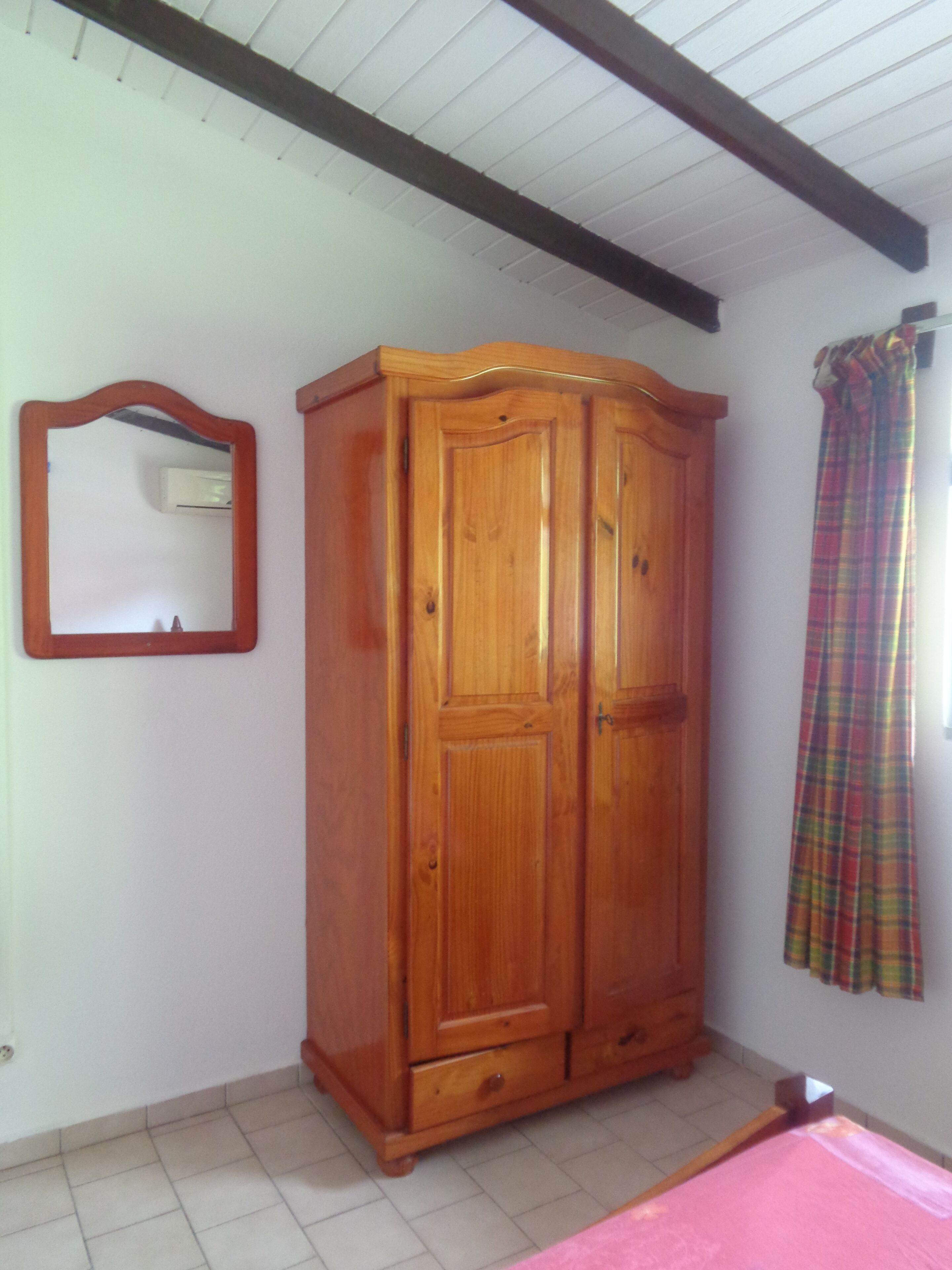 A room with a wooden wardrobe, a mirror, and a plaid curtain.