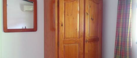 A room with a wooden wardrobe, a mirror, and a plaid curtain.