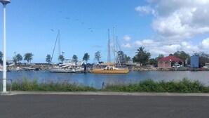 Un puerto deportivo con varias embarcaciones amarradas, un pequeño edificio de techo rojo y un cielo despejado.