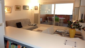 A modern living room with a sofa, a dining table with chairs, a small kitchen area, and a sliding glass door leading to an outdoor patio. - <--Right on this BEACH, Bright 1-Bedroom Apartment; OCEAN VIEW. ****42 m² + TERRACE + garage + Wi-Fi (Capbreton)