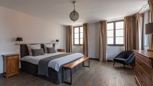 A bedroom with a large bed, a wooden bench, a chair, a dresser, and a hanging light fixture. - Superb 18th century farmhouse, in the heart of the vineyard. (Epfig)