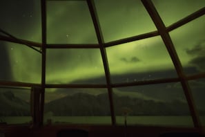 A room with a large window offering a view of a mountainous landscape and a body of water. - Lyngen North (Nordreisa)