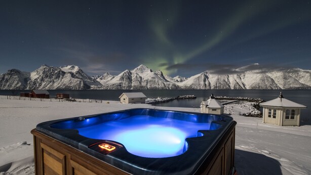 Un bain à remous dans un paysage enneigé, avec des montagnes et un ciel nocturne dégagé.