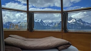 Un lit donnant sur des montagnes enneigées, vue par une fenêtre.