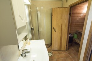 A bathroom with a white sink, a glass shower enclosure, and a wooden door leading to a storage area. - Lyngen North (Nordreisa)