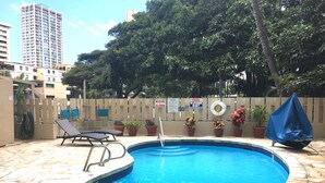 Une petite piscine ronde, bordée de pierres, entourée de plantes en pot et d’une clôture.