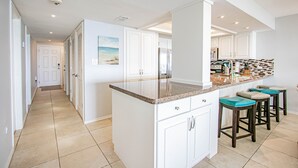 A modern kitchen with white cabinets, a granite countertop, and a view of the beach through the window. - Walls of windows overlooking the blue ocean!  (South Padre Island)