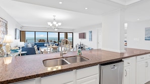 A modern kitchen with granite countertops, stainless steel appliances, and a large window overlooking the ocean. - Walls of windows overlooking the blue ocean!  (South Padre Island)
